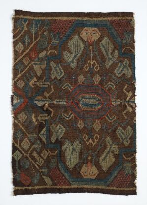  An intricately patterned rug or woven textile with a dark background and symmetrical, geometric patterns in earth tones and accented with occasional bright colors, potentially of traditional or ethnic origin.