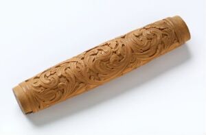  An intricately carved wooden cylindrical object with a floral pattern, resting on a light-colored background.