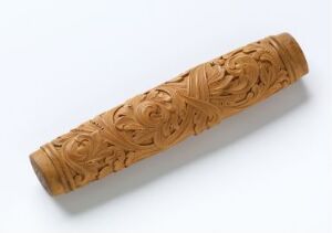  A cylindrical wood carving with intricate floral and leaf patterns on a plain white background.