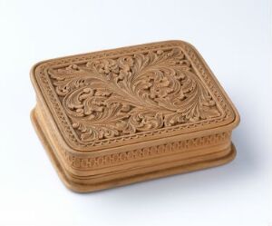  A rectangular light brown box with a floral embossed lid on a neutral gray background, showcasing a stylized, intricate design with a vintage appearance.