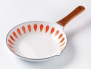  The "Lotus Omelettpanne" by Grete Prytz Kittelsen, an enameled steel omelet pan with a wooden teak handle, featuring a white interior with a decorative border of stylized reddish-orange lotus petals.