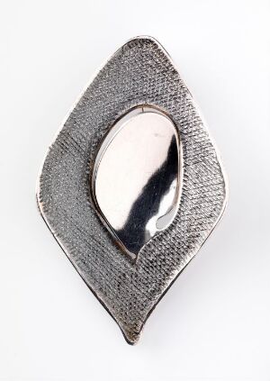  A silver breastplate jewelry piece entitled "Med speil" by Grete Prytz Kittelsen, with a textured, leaf-like design, featuring a central mirrored oval that reflects the light.