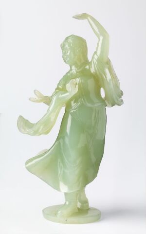  A translucent jade green figurine of a graceful, dancing woman with one arm extended above her head and the other to the side, standing on a round base, with light passing through varying depths of color on the smooth material. Artist name and title are unknown.