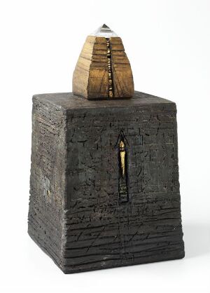  A crafted ceramic art piece titled "Kailas m. bergkrystall" by Kari Margrethe Christensen, depicting a square, textured stoneware base in deep charcoal black with a central keyhole-shaped golden-yellow opening, and an intricate layered brown pyramid top capped with a clear crystal.