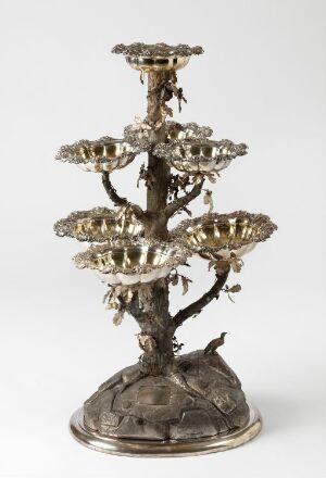  An elaborate multi-tiered silver candelabrum with a base mimicking textured tree roots, a trunk-like stem, and multiple branches with candle holders resembling floral elements.