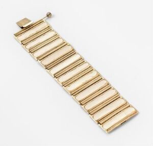  A gold-colored bracelet composed of linked cylindrical elements against a white background, reflecting a soft sheen indicative of a metallic, polished surface. Artist name and title are unknown.