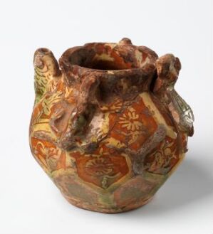  An ornately decorated ceramic pot with bulbous body, irregular open top, and two ornamental handles, featuring earthy tones of brown, tan, ocher, and muted red with patterns and figures suggestive of ancient artwork.