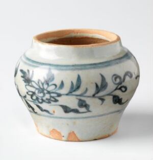  A small stout ceramic pot with a creamy base and traditional blue floral and foliate motifs around its circumference on a neutral background. The pot shows slight signs of wear at the rim and base, adding to its antique charm.