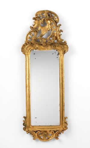  An antique vertical mirror with a golden baroque frame, adorned with intricate scroll and floral designs, against a plain white background.