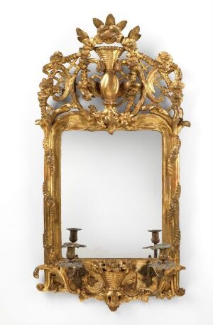  An ornate golden mirror with floral and leaf motifs sculpted into the frame, an urn-like crest at the top, and two candlestick holders at the base, set against a white background.