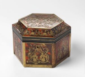  An antique hexagonal box with a floral-patterned lid in red, gold, whites, and blacks showcasing detailed scrollwork. The box’s sides feature similar intricate designs against a dark background, suggesting age and craftsmanship.