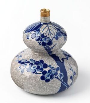  A double-gourd-shaped porcelain object intricately decorated with cobalt-blue floral motifs on a white glossy background with a small golden stopper on top. Artist name and title are unknown.