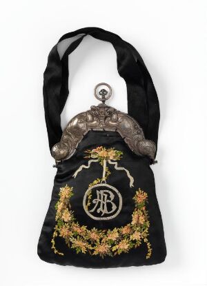  A vintage-style evening bag with a black satin strap and body, featuring an ornate aged silver metal clasp frame and a front design with a golden monogram surrounded by intricate embroidery in golds, oranges, and greens.