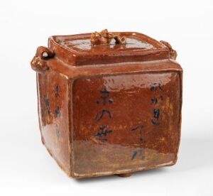  A small, cube-shaped, reddish-brown ceramic container with a glossy surface, featuring faded dark blue to black calligraphy or markings on its sides and a knob on the lid. Artist name and title are unknown.