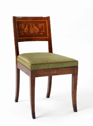  Antique wooden chair with three frolicking dogs carved into the backrest, upholstered with olive green fabric, set against a light background.