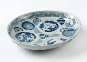  A shallow ceramic bowl with intricate blue patterns, including floral and abstract motifs, on a white background, indicative of traditional East Asian porcelain art. Artist name and title are unknown.