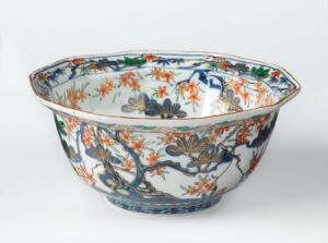  An ornately decorated ceramic bowl with a white background and a colorful floral pattern including vibrant oranges, blues, greens, and reds, with dark branches interconnecting the elements.