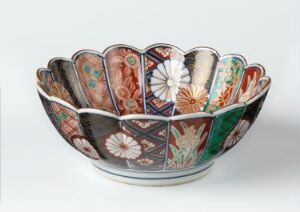  An intricately patterned bowl with overlapping fan-like segments, each adorned with unique colorful designs, resembling a flower in bloom, against an off-white background.