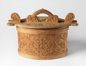  A delicately carved wooden basket with ornate geometric and floral patterns and a looped, central handle on top, set against a white background. The wood is a light honey-brown color, and the craftsmanship suggests a traditional or cultural significance.