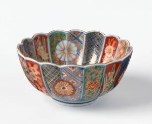  An intricately decorated, scallop-edged bowl featuring segmented patterns of floral and geometrical designs in vivid shades of orange, green, blue, and red on an off-white background, suggesting traditional Eastern craftsmanship.