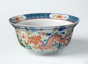  An ornate ceramic bowl with a dragon and floral design, featuring vibrant shades of orange, blue, green, and yellow on a white background.