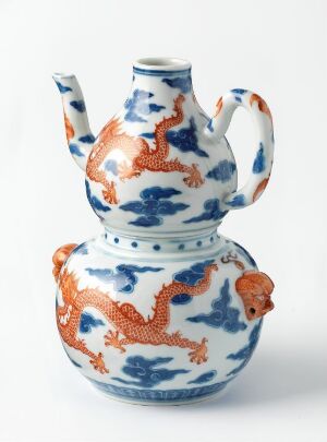  A white porcelain ewer decorated with cobalt blue patterns and raised orange dragons, featuring a curvy handle and tall spout, indicative of traditional East Asian design.