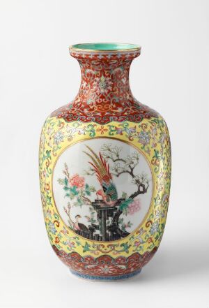  An ornate ceramic vase with a glossy finish, featuring a busy floral pattern with reds, greens, and yellows on the neck and base, and a central oval panel depicting a serene East-Asian landscape scene surrounded by decorative borders.