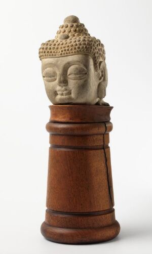  A sculpture combining a serene Buddha head, with a light, sandy color indicative of marble or sandstone, atop a wooden chess rook in a rich, warm brown tone, possibly representing a blend of spirituality and traditional gaming elements.