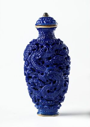  An ornate cobalt blue vase with a gold-trimmed neck and lid, featuring elaborate raised relief baroque design patterns all over its surface, set against a neutral off-white background.