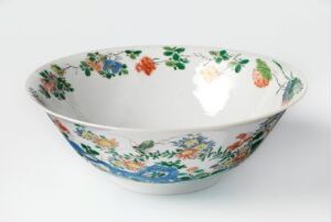  A white ceramic bowl with a colorful floral pattern in blue, green, red, orange, and yellow, intricately designed on both the interior and exterior. The bowl rests on a light grey background.