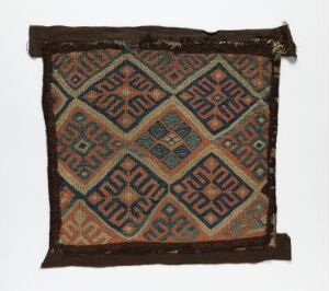  An antique geometric patterned textile featuring a brown background with complex diamond shapes in teal, burnt orange-red, and black, showing wear and uneven edges. Artist name and title are unknown.