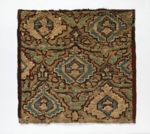  An antique square textile with intricate geometric designs in teal, cream, black, rust-orange, and brown, showing signs of wear along the edges.