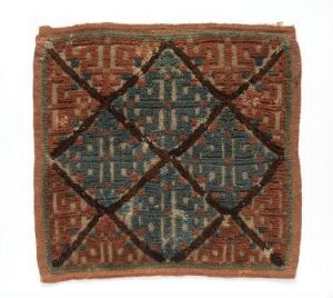  Antique square textile with a central diamond pattern in faded teal surrounded by terracotta geometric designs, showcasing signs of age and traditional craftsmanship.