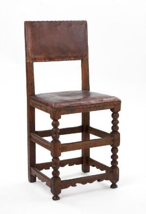  An antique wooden chair with a warm chestnut brown color, featuring a rectangular backrest, a flat plank seat, and turned legs and stretchers, set against a light-colored background.