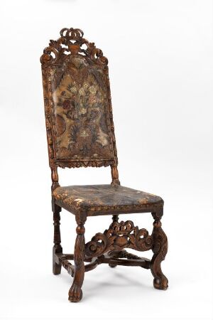  An antique wooden chair with a tall, ornately carved backrest featuring a floral tapestry in muted tones and clawed feet, set against a neutral background.