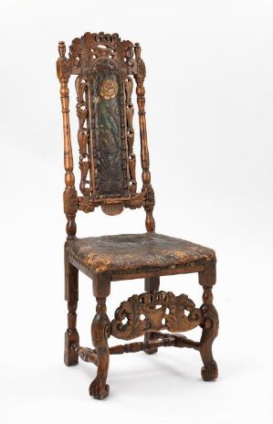  An antique wooden chair with elaborate carvings, featuring scrolled and floral patterns, a decorative central medallion on the backrest, and ornate legs with cross braces, set against a plain background.