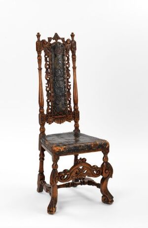  An elaborately carved, dark mahogany wooden chair with a high back and intricate scroll and leaf designs, featuring a dark upholstered seat and back panel, set against a backdrop that transitions from white at the bottom to light gray at the top.