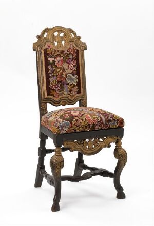  An antique, ornately carved wooden chair with claw-and-ball front legs and a tall, open-frame backrest, upholstered with a colorful floral tapestry.