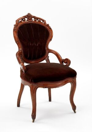  An elegant antique mahogany chair with a tufted velvet backrest and seat, featuring ornate wood carvings and curving cabriole legs against a plain background.