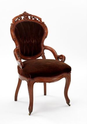  An antique Victorian-style chair with intricate wood carvings and deep brown velvet upholstery, set against a white background.