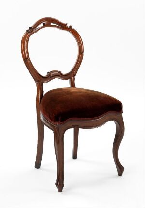  An antique-style chair with a looped backrest and deep brown wooden frame, featuring chocolate velvet upholstery on the seat, against a plain background. Artist and title unknown.