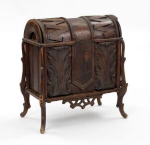  A small, antique-looking wooden chest with a curved top sits on a crafted wooden stand, featuring intricate leaf-like carvings with a deep and warm brown color palette set against a light, neutral background. Artist unknown.