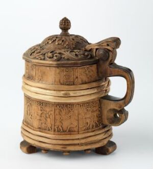  An intricately carved cylindrical wooden tankard with a decorated lid and handle, showcasing detailed relief work including foliate patterns and possibly historic or storytelling scenes, set against a light gray background.