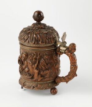  An intricately designed, brown relief stein with a detailed forest scene and a figure, featuring an ornamental lid and a vine-like handle.