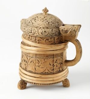  An intricately carved wooden teapot with detailed botanical motifs, presented on a carved, circular base against a plain, off-white background. The teapot exhibits a warm honey-colored wood grain, showcasing exceptional craftsmanship.