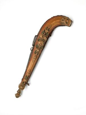  An intricately carved horn with decorative motifs and a metal tip, featuring a deep warm brown color and lighter colored embellishments against an off-white background.