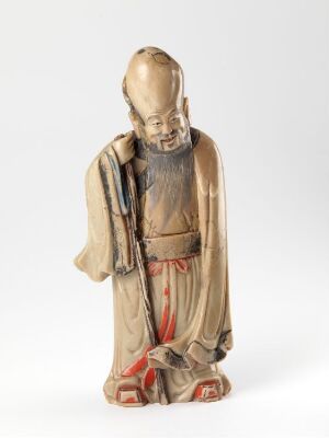  An intricately detailed statuette of an elderly, meditative figure in a flowing beige and red-accented robe, with closed eyes and a contemplative pose, holding a staff, on a neutral background. Artist name and title unknown.