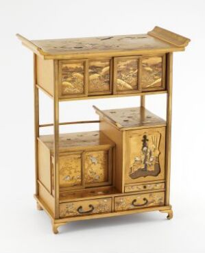 
 An ornate golden-brown wooden cabinet with intricate panels and artwork, featuring multiple drawers and levels, and a polished finish indicative of an antique style.