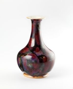  A glossy, iridescent vase with a rounded body and narrow neck, predominantly maroon with swirls of dark blue and indigo, set against a plain white background. Artist name and title remain unknown.