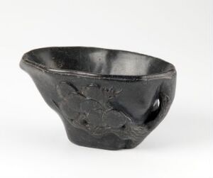  A glossy black ceramic bowl with an uneven, organic shape and a raised floral design on its exterior, resting against a light gray background.